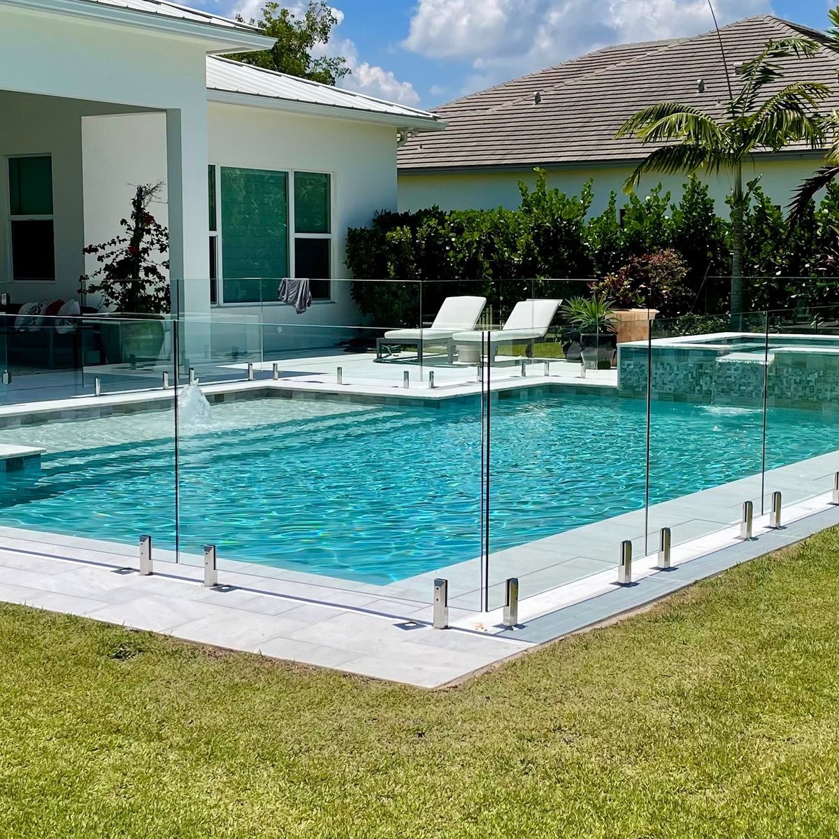 Frameless glass pool fence surrounding a backyard pool with lawn and sun lounges